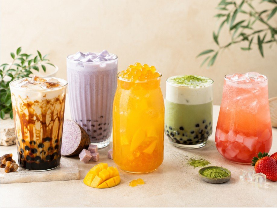 Five colorful boba drinks including brown sugar milk, taro milk tea, mango fruit tea, matcha boba, and strawberry jelly tea